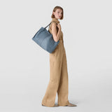 Side view: SECRET TOTE BAG IN CACHEMIRE LEATHER AND MOSAICO worn over the shoulder of a standing woman, indigo cachemire leather with visible Mosaico detail against a neutral background.