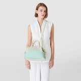Front view: Model wears ANI BAG IN MOSAICO MESTIERI D'ARTE over the shoulder, small bauletto shape with cream handles and pastel Bokashi mosaic pattern, neutral background.