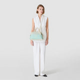 Frontal view: Model wears ANI BAG IN MOSAICO MESTIERI D'ARTE over her shoulder and holds the handles, pastel green-light beige Bokashi leather, against a neutral light gray background.