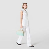 Side view: The ANI BAG IN MOSAICO MESTIERI D'ARTE is carried by hand while a model in a white ensemble walks against a light, neutral background.