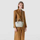 Front view: Model wears MINI SECRET BAG IN MOSAICO AND ELAPHE on an adjustable shoulder strap; it hangs at the side of the body, showing the delicate Mosaico weave.