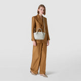 Front view: model wears MINI SECRET BAG IN MOSAICO AND ELAPHE across the shoulder; light grey patterned Mosaico leather bag rests on an elegant brown suit, showing the top handle and shoulder strap.