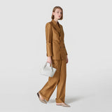 Frontal view: MINI SECRET BAG IN MOSAICO AND ELAPHE is held in the right hand, presented on a model standing sideways against a plain light gray background.