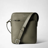 Frontal view: NORTH SOUTH CROSSBODY BAG IN CACHEMIRE LEATHER, standing upright against a light background, adjustable shoulder strap positioned diagonally, pebbled Leaf cachemire leather, visible 'SERAPIAN MILANO' logo print and front zipper.