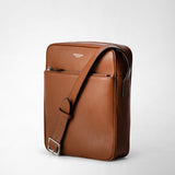 Front view: NORTH SOUTH CROSSBODY BAG IN CACHEMIRE LEATHER — brown, flat crossbody bag standing upright with adjustable strap positioned diagonally, on a light background; front zip pocket and visible 'SERAPIAN MILANO' logo.