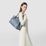 Side view of a woman carrying the SMALL SECRET TOTE BAG IN CACHEMIRE LEATHER AND MOSAICO in storm blue with Mosaico details casually over her shoulder.