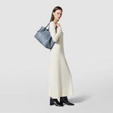 Side view of a woman carrying the SMALL SECRET TOTE BAG IN CACHEMIRE LEATHER AND MOSAICO in Storm blue with Mosaico details over her shoulder.