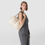 Side view: Model wears SMALL SECRET TOTE BAG IN CACHEMIRE LEATHER AND MOSAICO casually over the shoulder; cream-colored, soft Cachemire leather with central Mosaico pattern and comfortable top handles against a neutral background.
