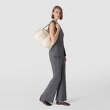 Side view: SMALL SECRET TOTE BAG IN CACHEMIRE LEATHER AND MOSAICO, cream-colored, with Mosaico details, worn on the shoulder of a woman standing in profile against a neutral background.