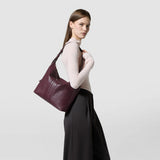 Side view of a woman carrying a grape ANI SHOULDER BAG IN CACHEMIRE LEATHER AND MOSAICO with adjustable shoulder strap over her shoulder.