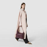 Side view: ANI SHOULDER BAG IN CACHEMIRE LEATHER AND MOSAICO is shown worn by a woman walking, displaying its grape-colored leather body and adjustable shoulder strap.