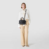 Front view: SMALL MARO BAG IN CACHEMIRE LEATHER AND MOSAICO hangs crossbody over the shoulder of a model facing forward, hands in pockets, neutral light studio background.