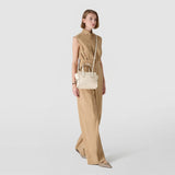 Front view: SMALL MARO BAG IN CACHEMIRE LEATHER AND MOSAICO — cream-colored mini handbag with nappa leather knot, two handles and a long shoulder strap, worn by a standing woman against a light background.
