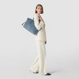Side view: Model wears MEDIUM MARO BAG IN CACHEMIRE LEATHER AND MOSAICO over the shoulder; indigo-blue Mosaico, knotted nappa leather strips, neutral background.