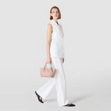 Side view: MINI SECRET BAG IN MOSAICO MESTIERI D'ARTE is carried by a woman in a white outfit on short handles as she walks against a light, neutral background.