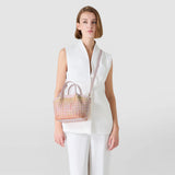 Front view — MINI SECRET BAG IN MOSAICO MESTIERI D'ARTE: small handbag with bokashi-pink mosaic pattern, two handles and a removable shoulder strap, worn crossbody on a model dressed in white.