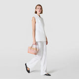 Frontal view: MINI SECRET BAG IN MOSAICO MESTIERI D'ARTE — woman holds the small Bokashi-pink bag by its short handles next to a white pantsuit against a light studio background.