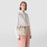 Frontal view: Model wears MINI SECRET BAG IN MOSAICO MESTIERI D'ARTE over the shoulder; cream mini bag with a pastel geometric mosaic, short handles and a long shoulder strap.