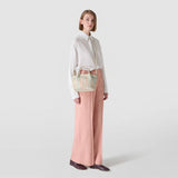 Front view: Model wears MINI SECRET BAG IN MOSAICO MESTIERI D'ARTE over the shoulder; small cream woven handbag with pastel mosaic pattern, held at the hip, neutral studio background.