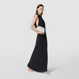 Front view: A woman holds the cream-colored MINI SECRET CLUTCH BAG IN MOSAICO MICROCHAIN in front of her black evening dress; the woven pattern is clearly visible.