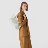 Side view: Model wears SMALL SECRET TOTE BAG IN MOSAICO AND ELAPHE over her shoulder; white Mosaico nappa leather bag with geometric woven pattern and Elaphe inserts, neutral background.