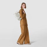 Side view: SMALL SECRET TOTE BAG IN MOSAICO AND ELAPHE worn over the shoulder; a white, mosaic-patterned leather bag with Elaphe inserts on a model in a brown pantsuit.