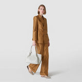 Front view: Woman carries SMALL SECRET TOTE BAG IN MOSAICO AND ELAPHE, holding it by the handles; light grey woven Mosaico texture with Elaphe inserts, neutral studio background.