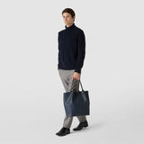 Front view of a man holding the VERTICAL SECRET TOTE BAG IN STEPAN in Ocean Blue. The bag features black leather handles and a subtle textured pattern.
