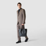 Front view of a man in a suit holding the VERTICAL SECRET TOTE BAG IN STEPAN in Asphalt Gray with black leather handles in his right hand.