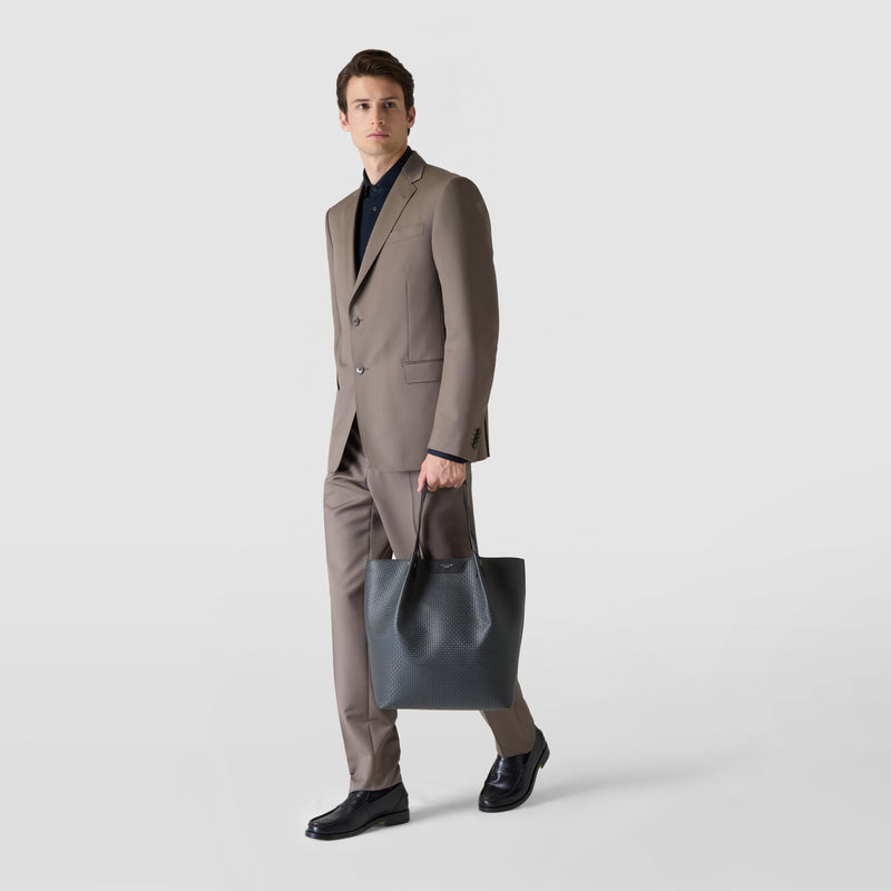 Front view of a man in a suit holding the VERTICAL SECRET TOTE BAG IN STEPAN in Asphalt Gray with black leather handles in his right hand.
